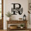 A black metal personalized monogram wall sign reading 'Reynolds' with ornate scrollwork, mounted on a beige wall above a wooden console table in a styled home entryway.