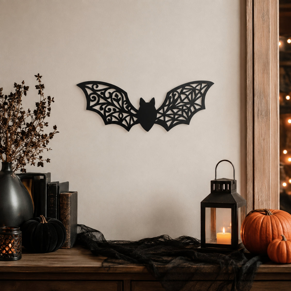 Black bat wall decor with intricate scrollwork wings, displayed on a beige wall above a styled wooden mantel with pumpkins, a lantern, and dried branches. Main image