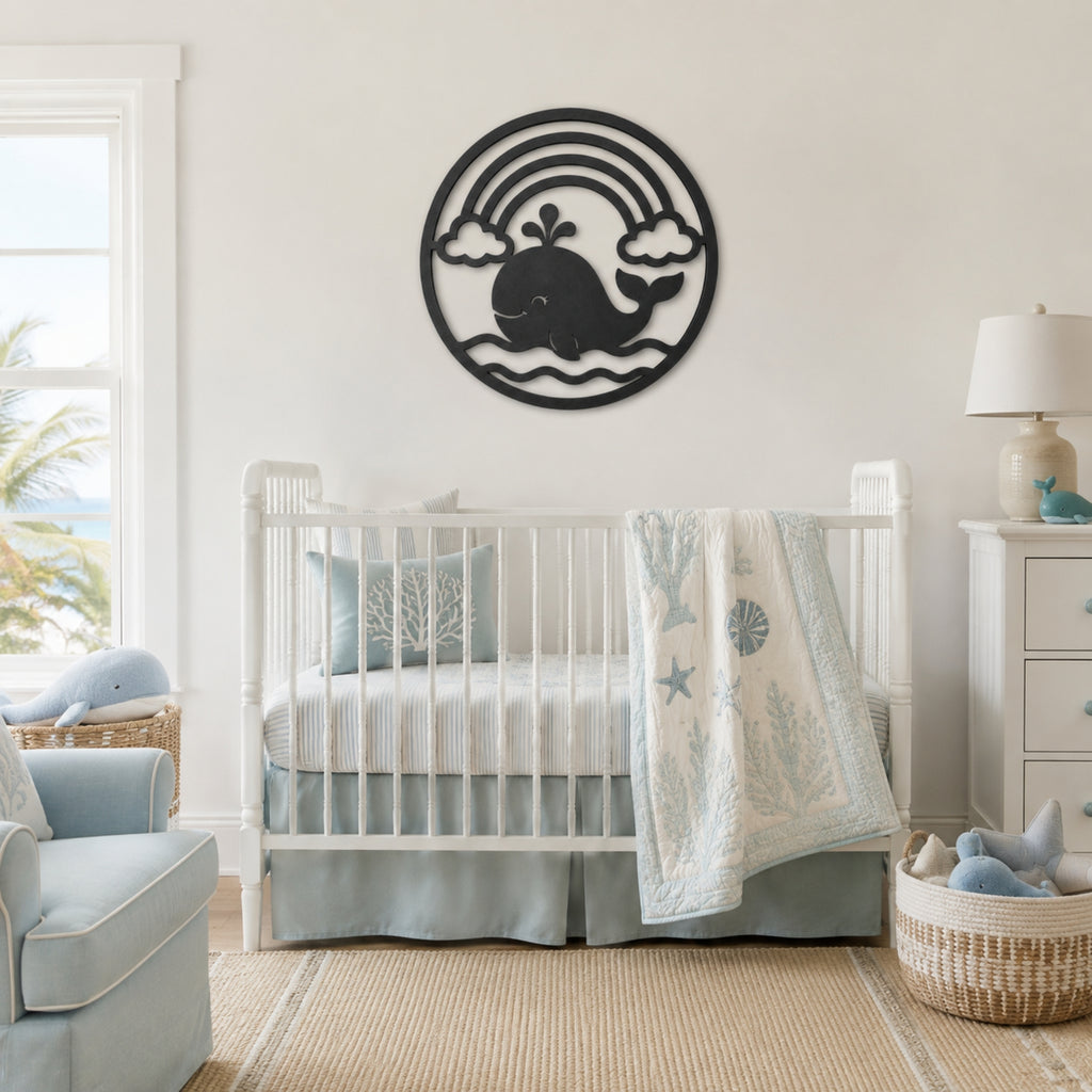 A white wooden crib in a bright, modern nursery with a light blue and white bedding set, a matching blue armchair, and a black metal whale wall art piece mounted on the wall above the crib.