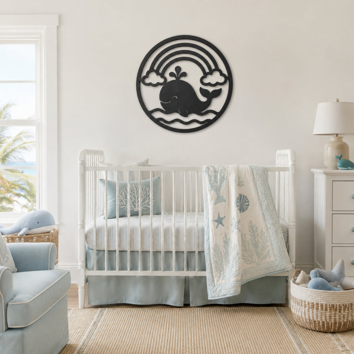 A white wooden crib in a bright, modern nursery with a light blue and white bedding set, a matching blue armchair, and a black metal whale wall art piece mounted on the wall above the crib.
