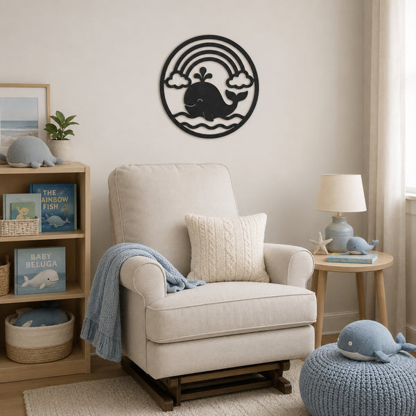 A styled nursery or playroom corner featuring a cream upholstered armchair with a cream cable-knit pillow and a light blue throw blanket. A wooden bookshelf on the left holds children's books and a gray whale plush, while a small wooden side table on the right holds a blue whale lamp and starfish.