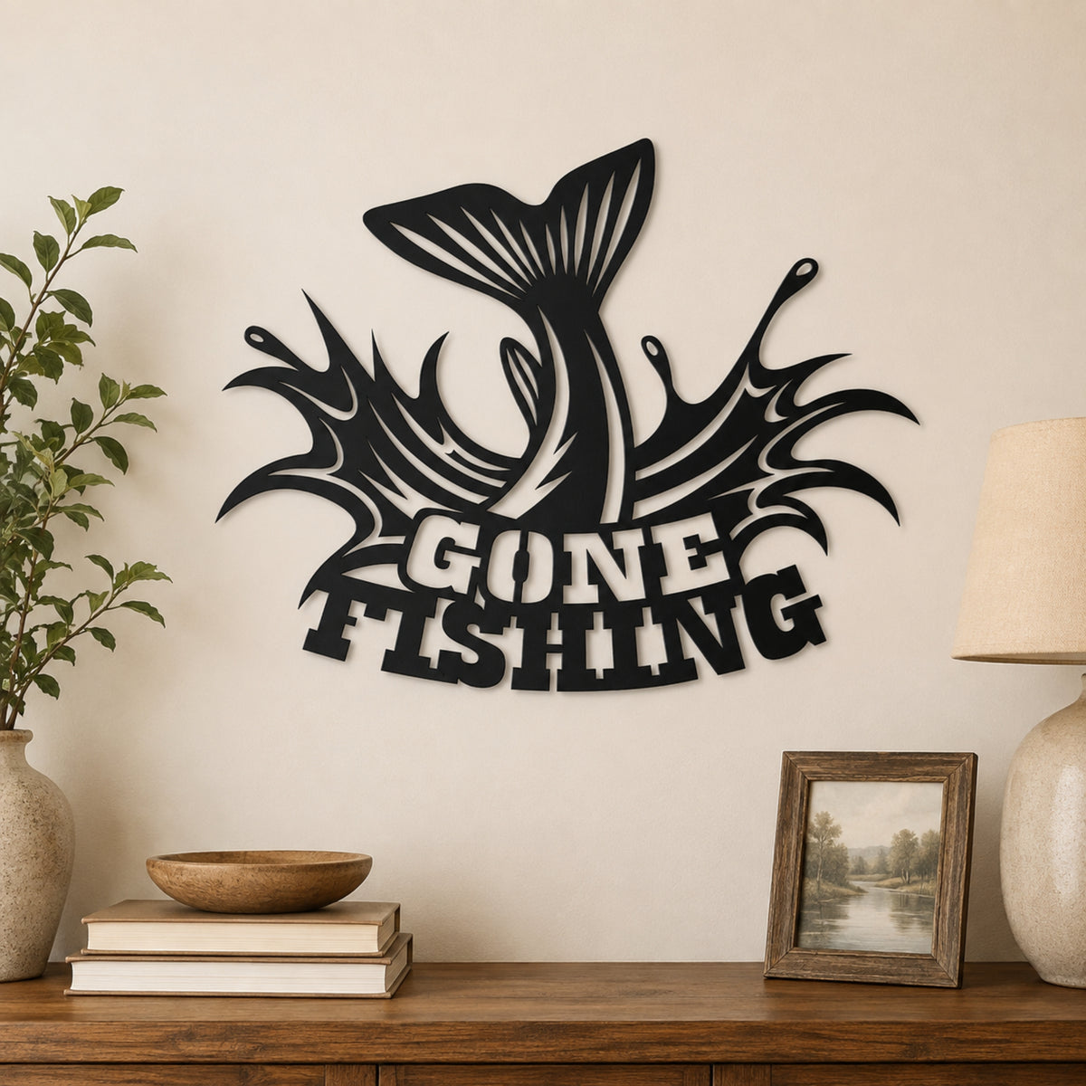 Black metal wall art featuring a jumping fish and the words 'GONE FISHING' in a stylized font, displayed on a beige wall above a wooden console table with books, a plant, and a lamp.