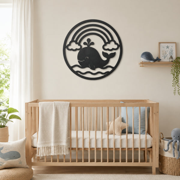 A black metal wall art piece featuring a whale, rainbow, and clouds, displayed above a light wood crib in a styled nursery room.