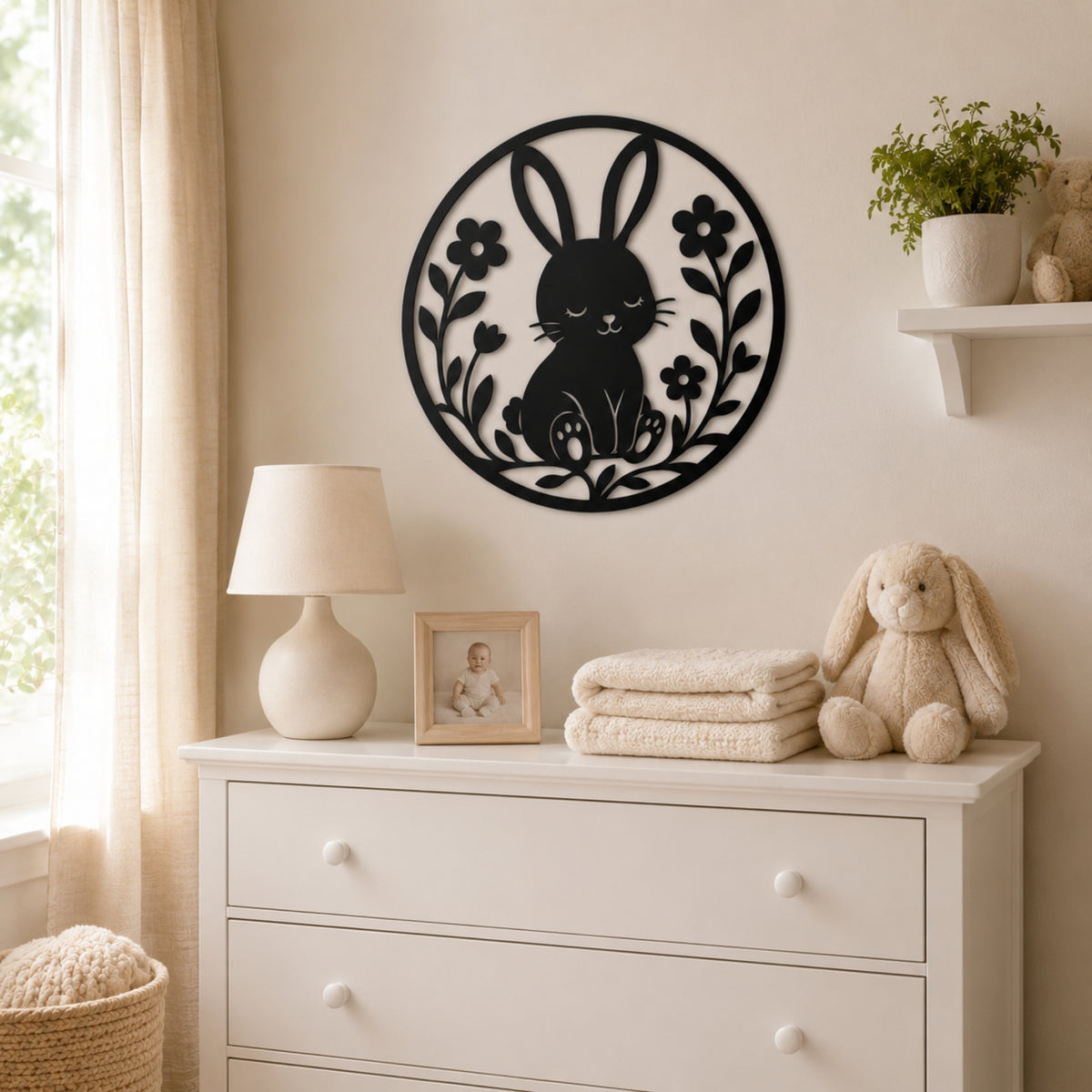 A black metal wall art piece featuring a bunny and floral design, displayed on a cream-colored wall above a white dresser in a styled nursery setting.