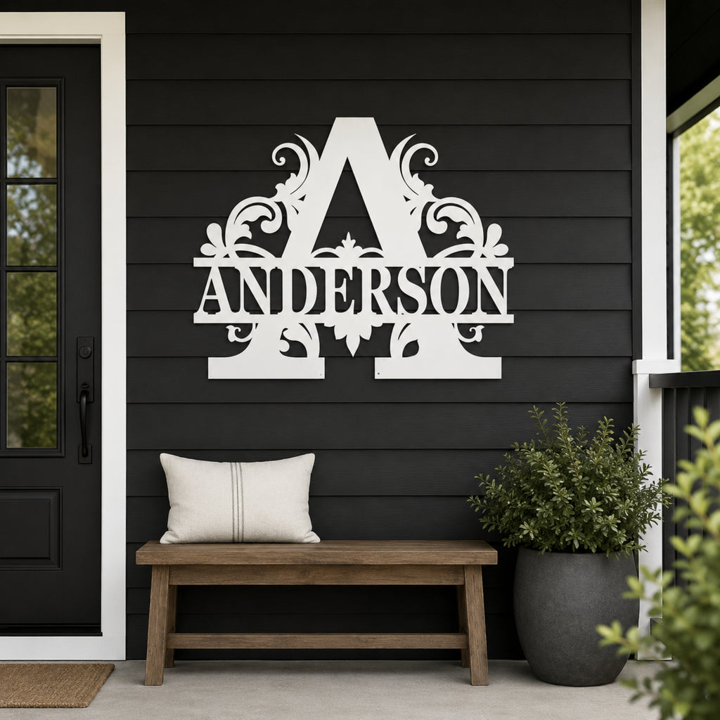 A white decorative metal wall sign featuring a large ornate letter A and the name ANDERSON, mounted on a black shiplap wall above a wooden bench with a white pillow on a porch.