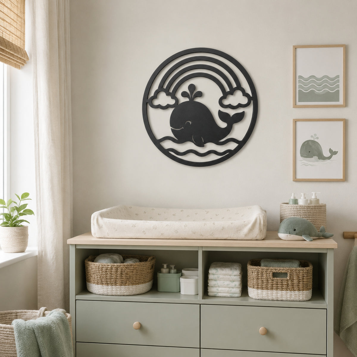 A styled nursery corner featuring a sage green changing dresser with woven baskets and a whale-shaped wall decor piece above it. The room has a soft neutral color palette with beige walls, a window with sheer curtains, and framed whale art prints on the wall.