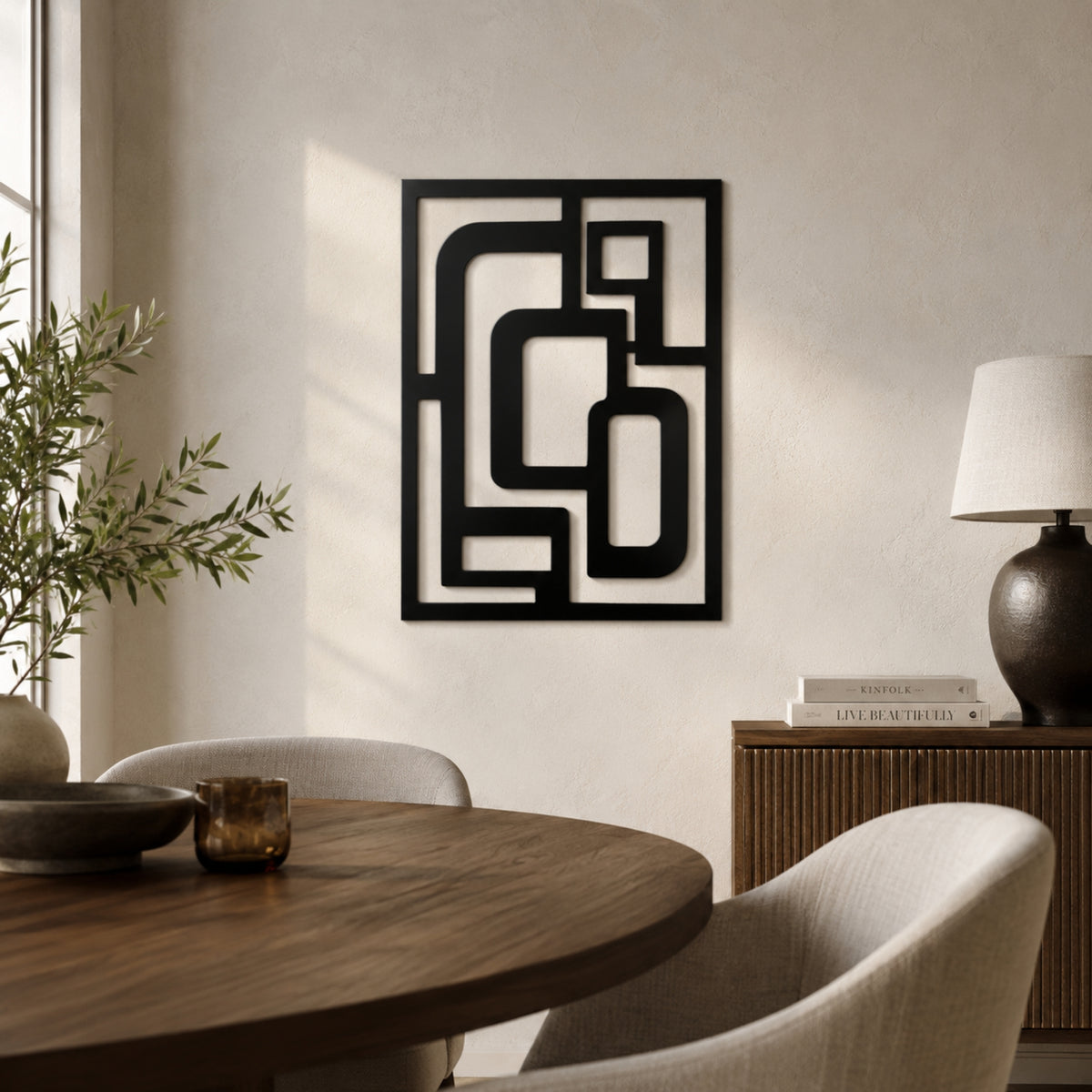 A black metal abstract geometric wall art piece hangs on a textured beige wall in a modern dining room setting with a wooden table, chairs, and a sideboard lamp.
