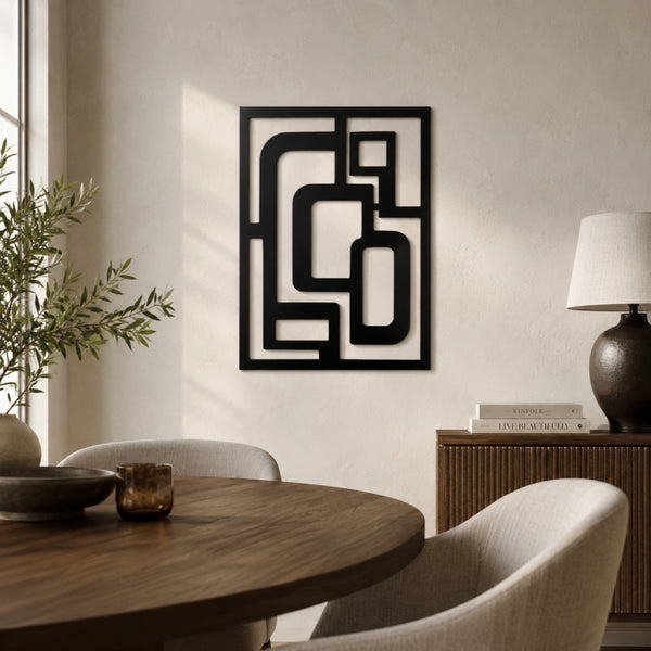 A black metal abstract geometric wall art piece hangs on a textured beige wall in a modern dining room setting with a wooden table, chairs, and a sideboard lamp.