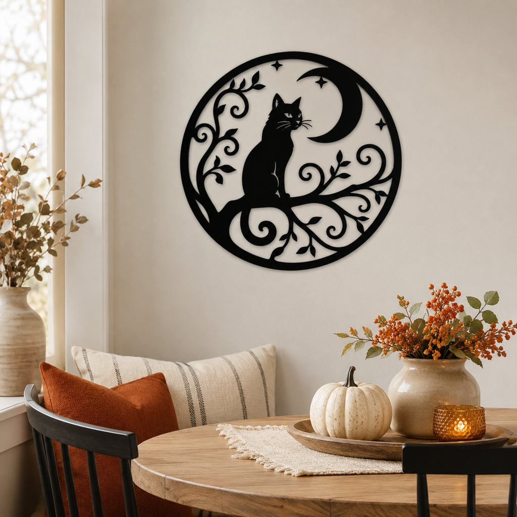 A black metal wall art piece featuring a cat silhouette on a branch with a crescent moon and stars, displayed on a beige wall above a wooden dining table with autumn decor.