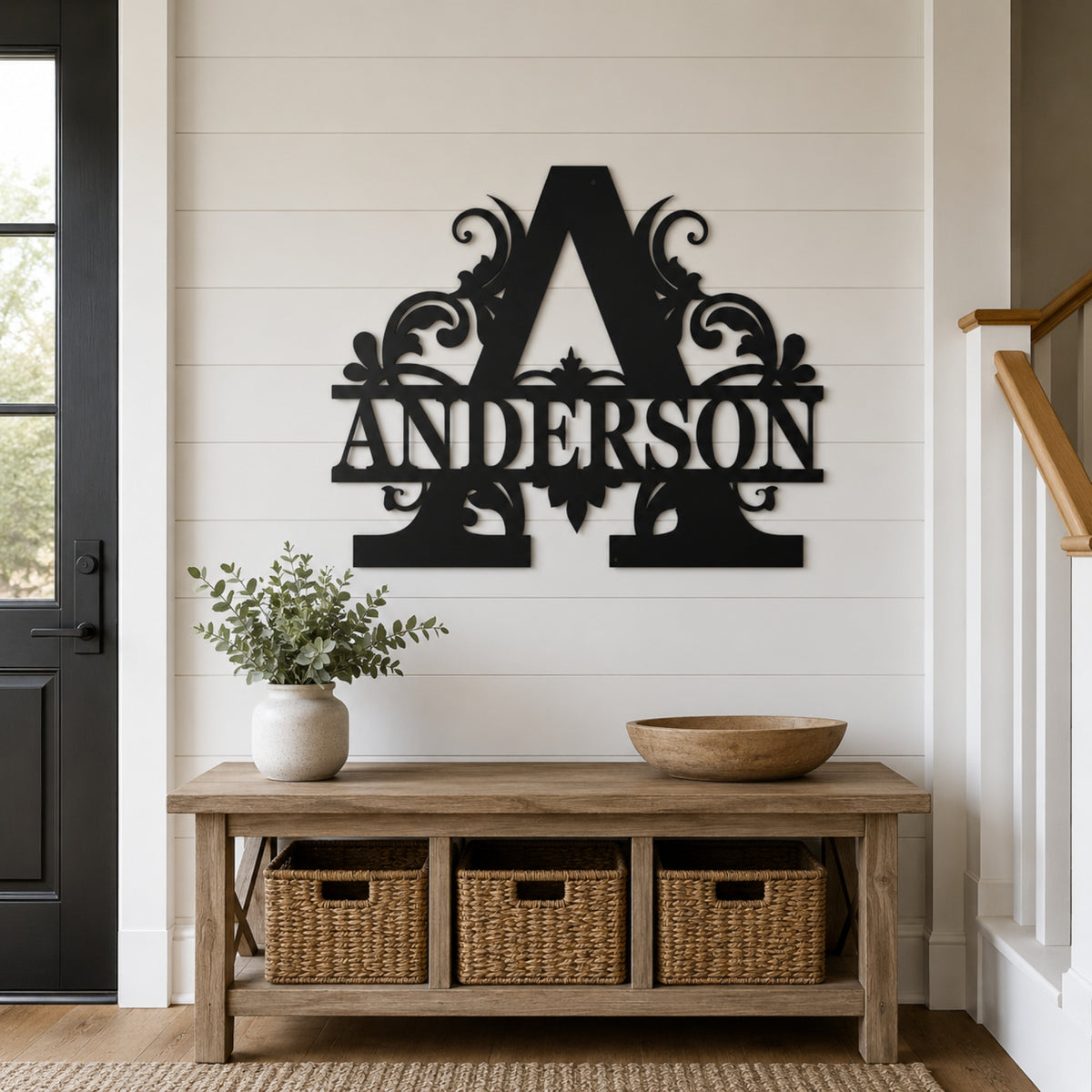 A black metal decorative wall sign featuring a large ornate letter A and the name ANDERSON, mounted on a white shiplap wall above a wooden bench with woven storage baskets in a styled entryway. Main image