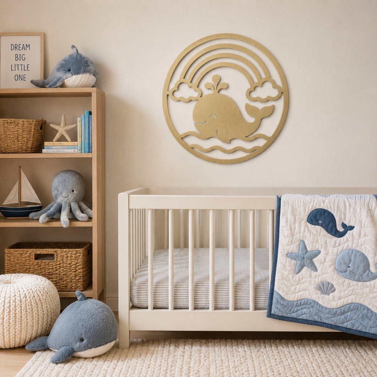 A styled nursery corner featuring a white wooden crib with a blue and white whale-patterned quilt, a light wood wall-mounted whale and rainbow decoration, a wooden shelf with toys, and a plush whale on a cream rug.