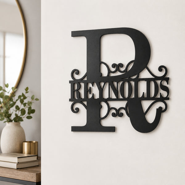 A black metal wall sign featuring a large decorative letter R with the name 'REYNOLDS' across the center, mounted on a white wall in a styled interior setting.