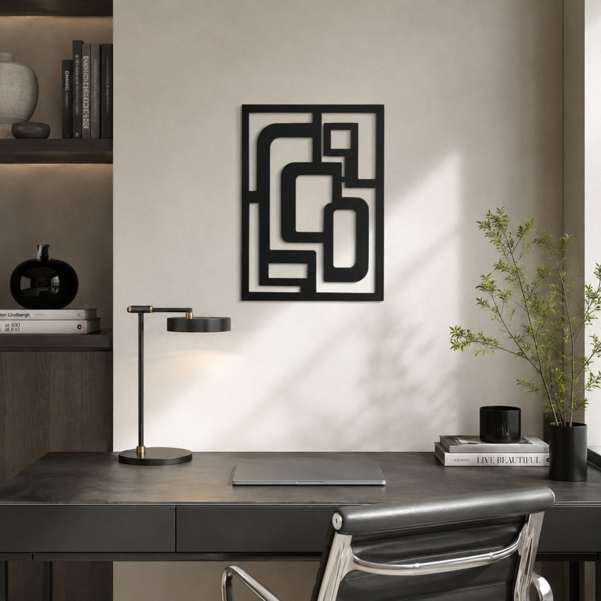 A modern black metal wall art piece with an abstract geometric pattern, displayed on a warm beige wall above a dark gray desk in a minimalist home office setting.