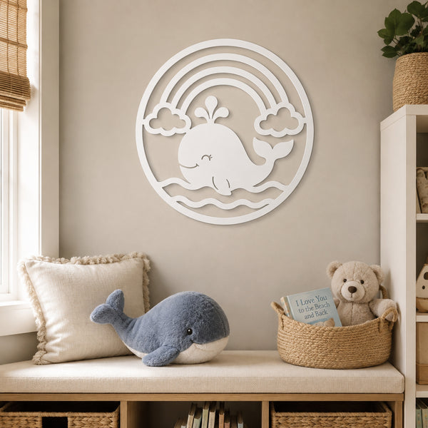 A white circular wall art piece featuring a whale, clouds, and rainbow arches, displayed on a beige wall above a cushioned bench with pillows, a plush whale, and a teddy bear in a nursery setting.