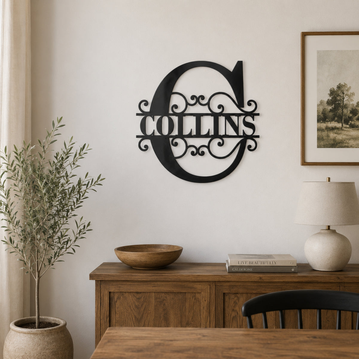 A black metal wall sign featuring a large decorative letter 'C' and the name 'COLLINS' in the center, mounted on a light beige wall above a wooden sideboard in a styled room setting.