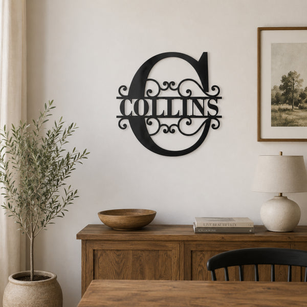 A black metal wall sign featuring a large decorative letter 'C' and the name 'COLLINS' in the center, mounted on a light beige wall above a wooden sideboard in a styled room setting.