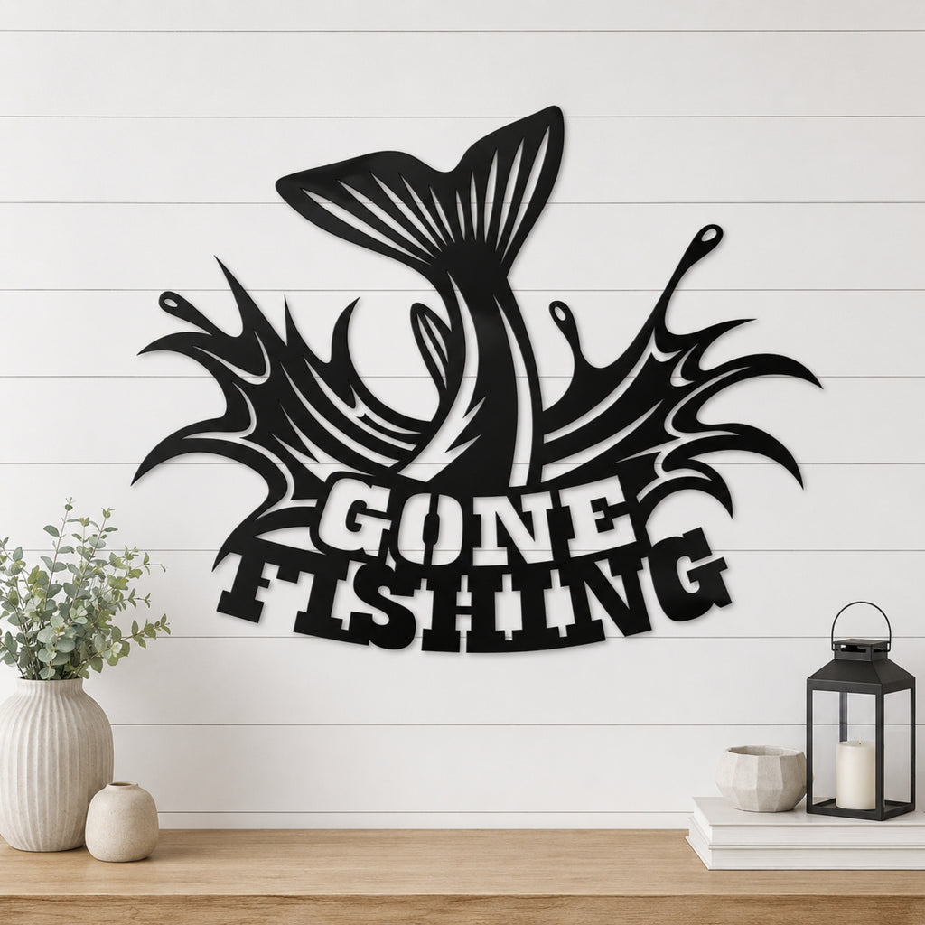 Black metal wall art featuring a leaping fish tail and the words “GONE FISHING” in a stylized font, mounted on a white shiplap wall above a wooden shelf with decorative vases, books, and a lantern.