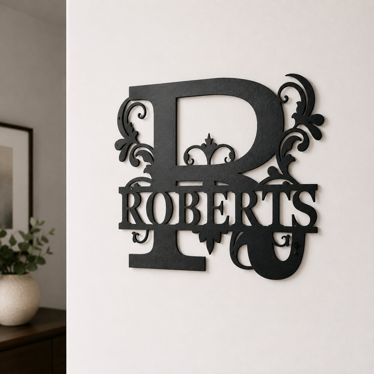 A black metal wall decor piece featuring a large ornate letter R and the name ROBERTS, mounted on a white wall in an indoor setting.