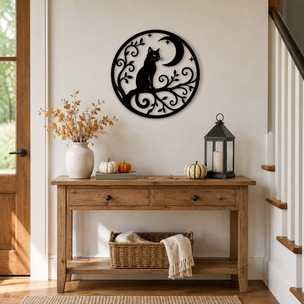 A black metal wall art piece featuring a cat silhouette around a crescent moon and scrollwork, mounted on a beige wall above a rustic wooden console table decorated with pumpkins, a lantern, and a vase.