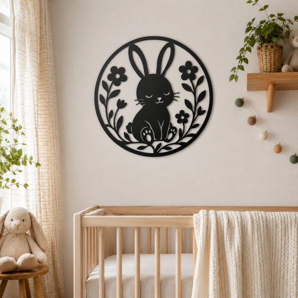 A black metal wall art piece featuring a bunny and floral design, displayed on a beige wall above a wooden crib in a softly styled nursery.