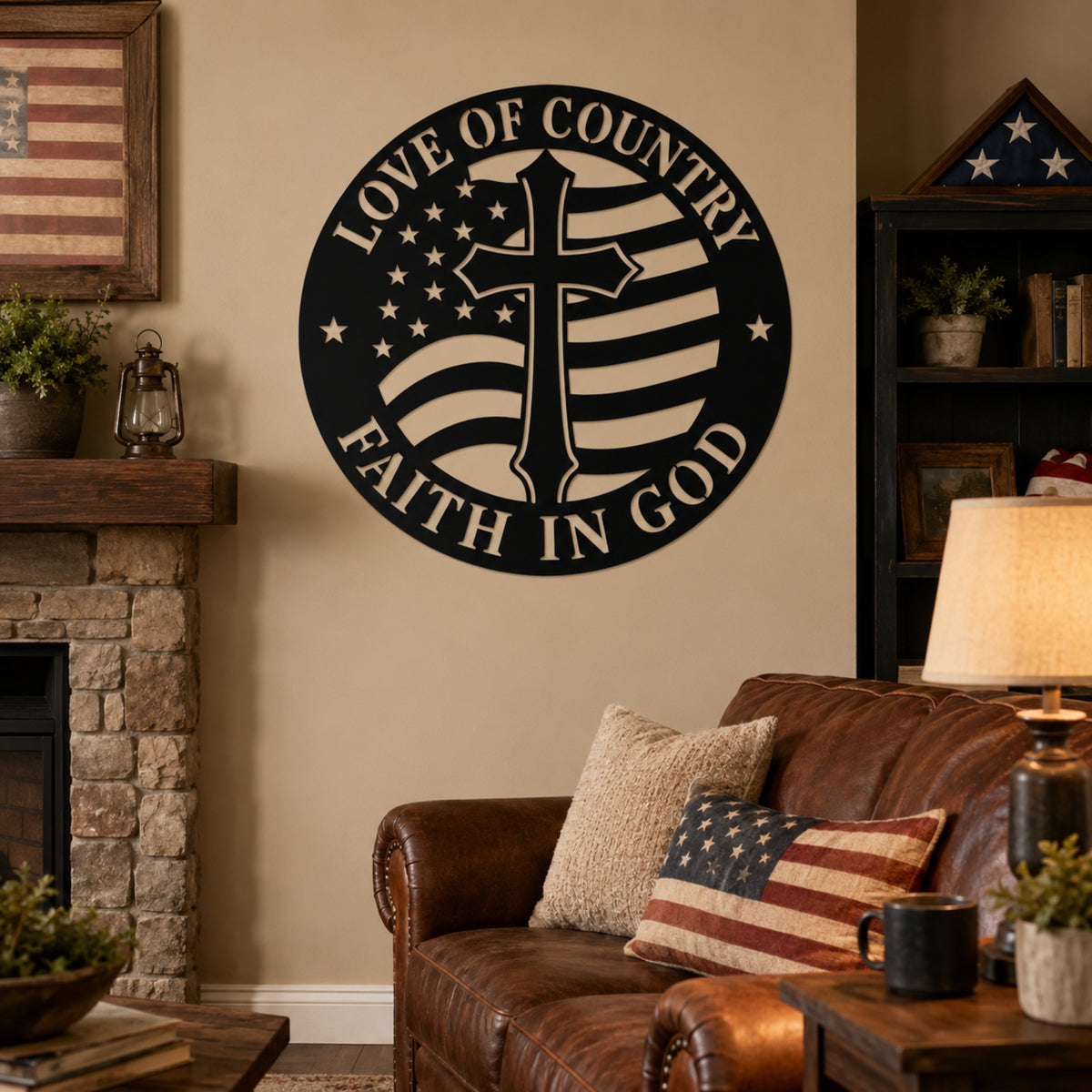 A round black metal wall sign featuring a central cross over an American flag design with the words 'LOVE OF COUNTRY' and 'FAITH IN GOD,' displayed on a beige wall in a living room above a brown leather sofa. Main image