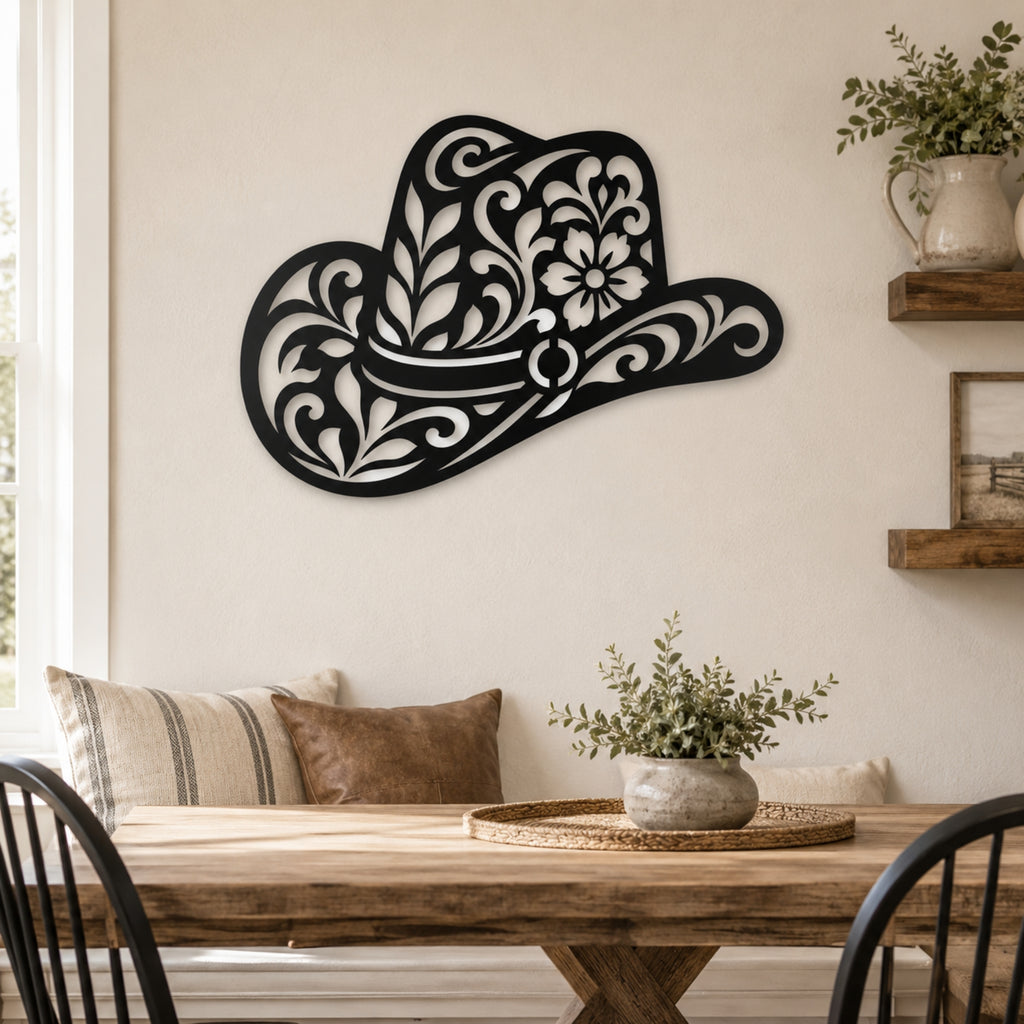 Black metal wall art shaped like a cowboy hat with ornate floral cutout details, displayed on a beige wall above a wooden dining table in a styled home interior.