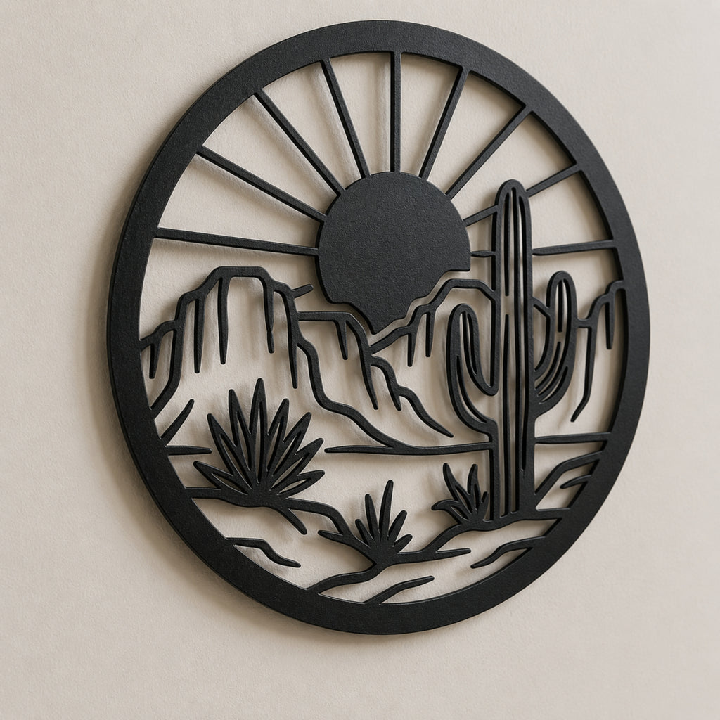 A circular black metal wall art piece featuring a desert landscape silhouette with a sun, mountains, saguaro cactus, and desert plants, mounted on a light beige wall.