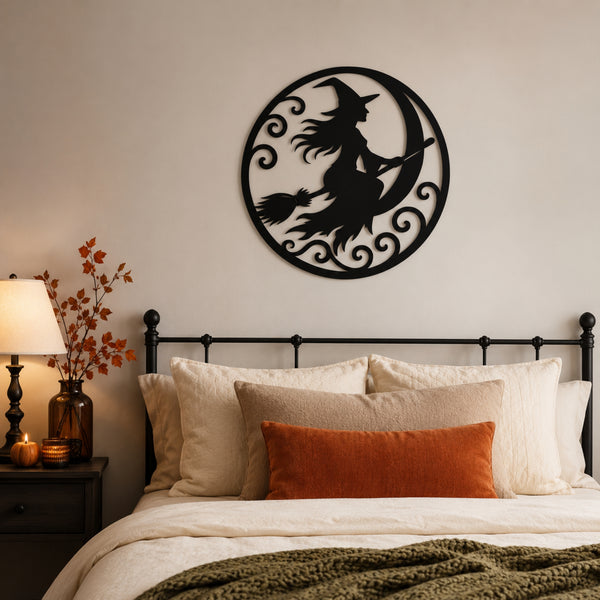 Black metal wall art featuring a witch riding a crescent moon, displayed above a bed in a cozy bedroom setting.
