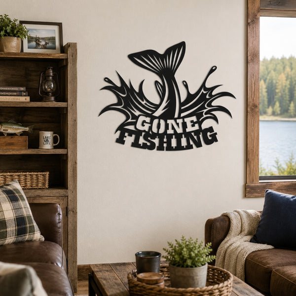 A black metal wall art piece featuring a jumping fish and the words 'GONE FISHING' is mounted on a beige wall in a rustic living room setting with a wooden bookshelf, leather sofa, and window overlooking a lake.
