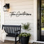 A black metal wall sign reading 'The Carters EST 1965' mounted on a white shiplap wall on a porch, with a black bench, potted plant, and front door visible.