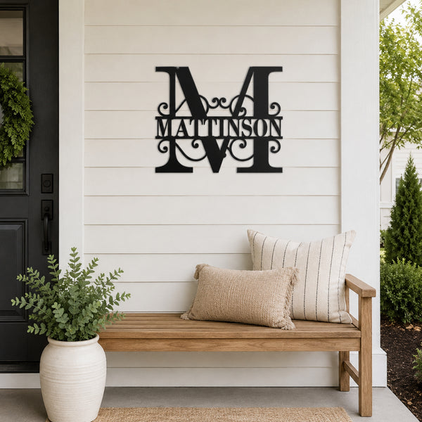 A black metal personalized wall sign featuring a large ornate monogram 'M' and the name 'MATTINSON' in the center, mounted on a white shiplap wall above a wooden bench with pillows in a front porch setting.