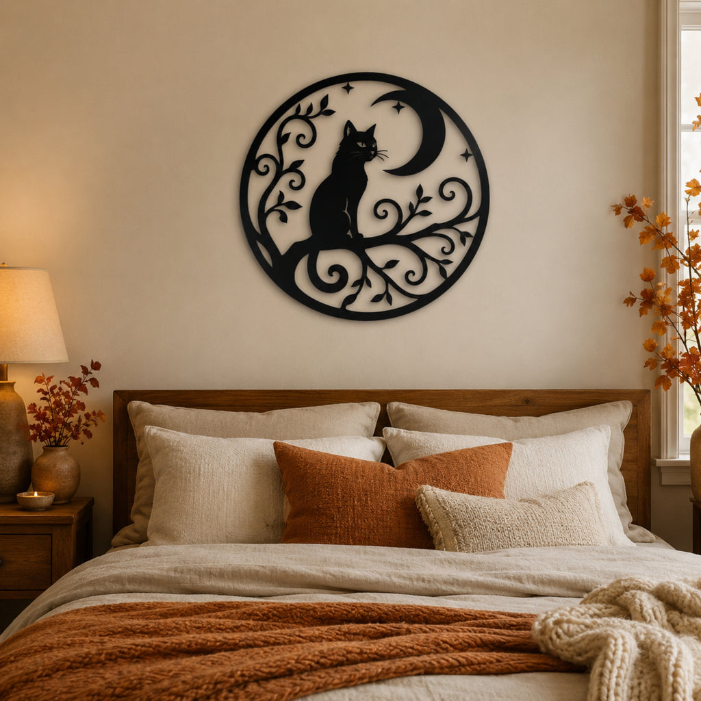 A circular black metal wall art piece featuring a cat silhouette sitting on a crescent moon and swirling branches, displayed above a bed in a warm, neutral-toned bedroom.