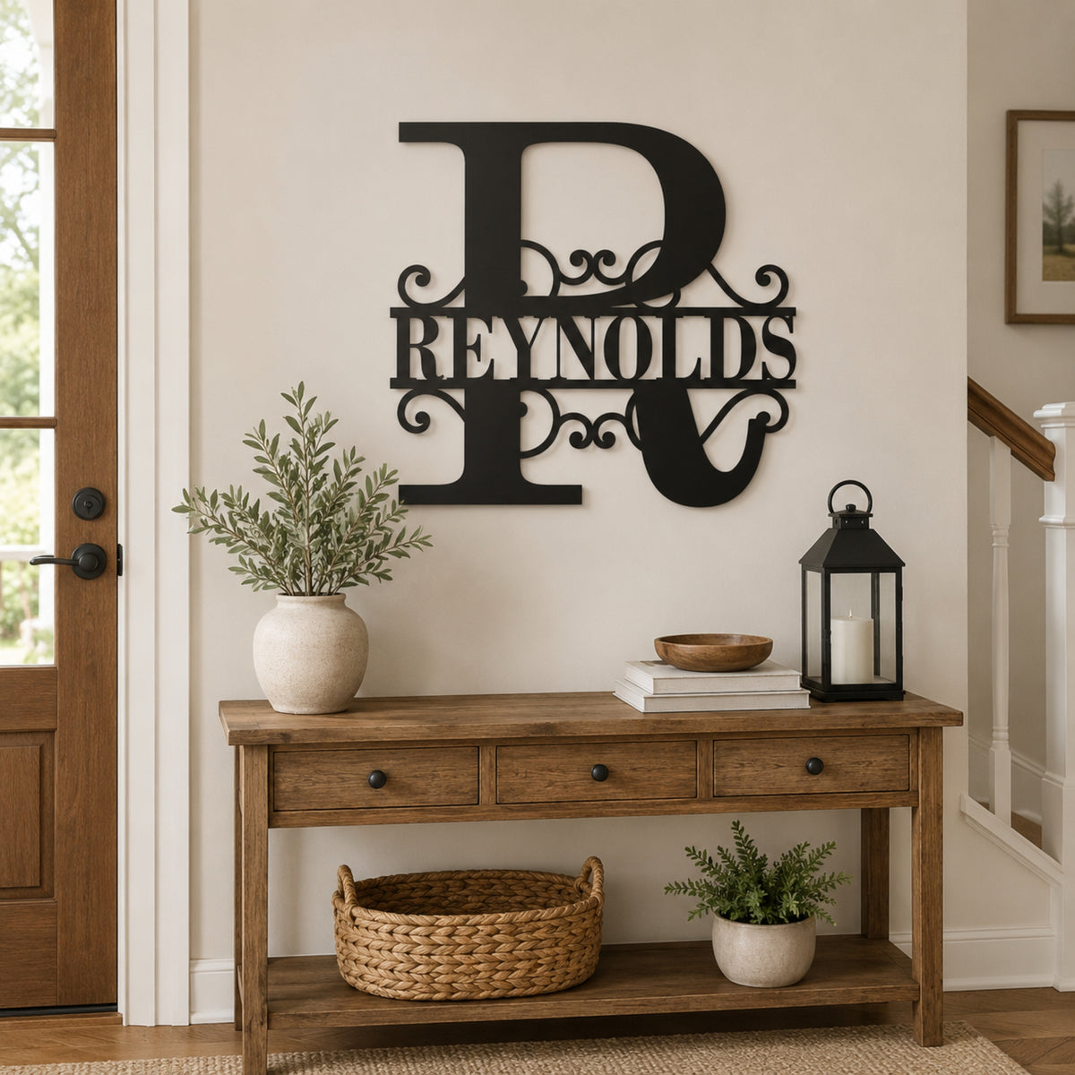 A black metal personalized monogram wall sign reading 'Reynolds' with ornate scrollwork, mounted on a beige wall above a wooden console table in a styled home entryway. Main image