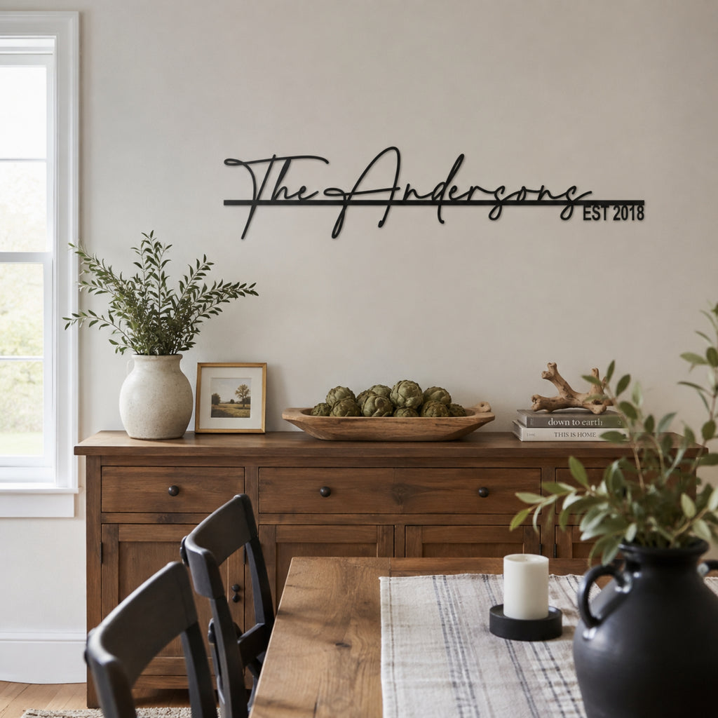 Custom black metal script wall sign reading 'The Andersons EST 2018' mounted on a beige wall above a wooden credenza in a styled dining room setting.