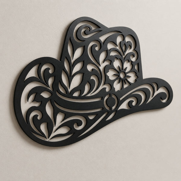 Black metal wall art shaped like a cowboy hat with ornate floral and scroll cutout details, mounted on a light beige textured wall.