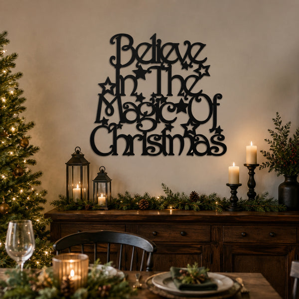 Black metal wall art with the phrase 'Believe in the Magic of Christmas' styled on a beige wall above a decorated holiday table with candles, pine garland, and a Christmas tree.