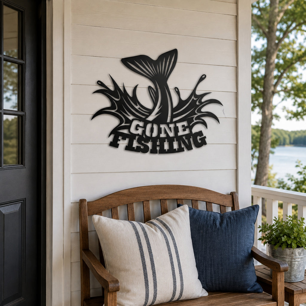Black metal wall art featuring a fish tail and the words 'GONE FISHING' displayed on a white shiplap wall above a wooden bench with decorative pillows on a porch.