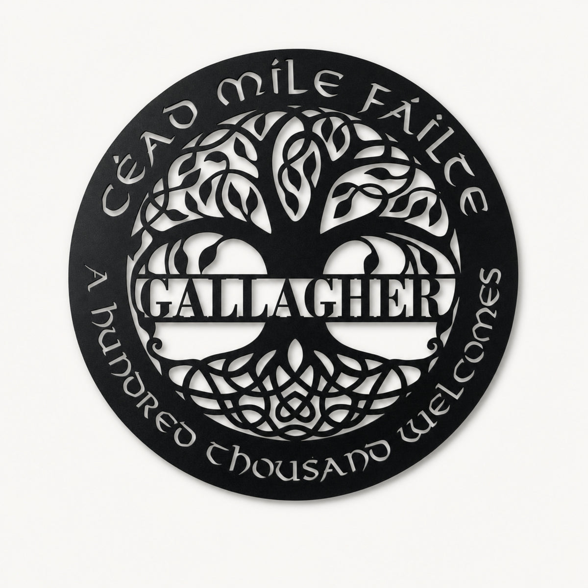 A circular black metal wall sign featuring a stylized tree of life with the name 'GALLAGHER' in the center, surrounded by the Irish phrase 'Éad míle féilte' and 'A hundred thousand welcomes' in white cutout lettering, shown on a light off-white background.
