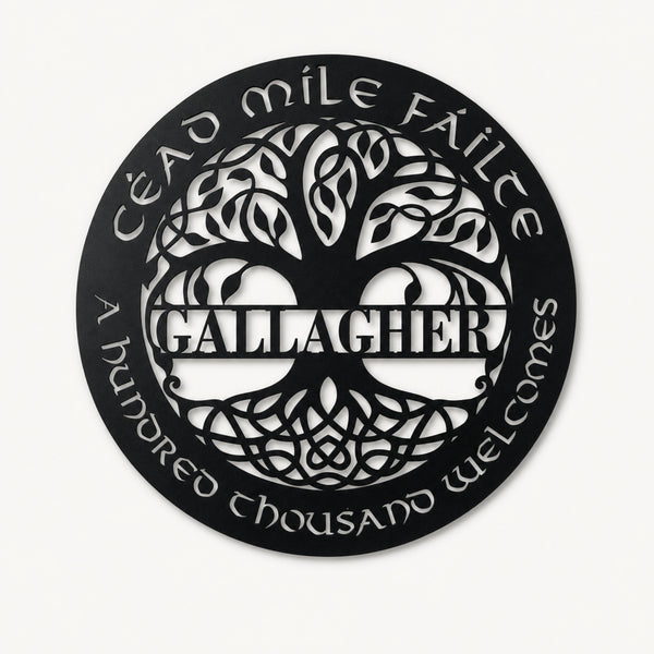 A circular black metal wall sign featuring a stylized tree of life with the name 'GALLAGHER' in the center, surrounded by the Irish phrase 'Éad míle féilte' and 'A hundred thousand welcomes' in white cutout lettering, shown on a light off-white background.