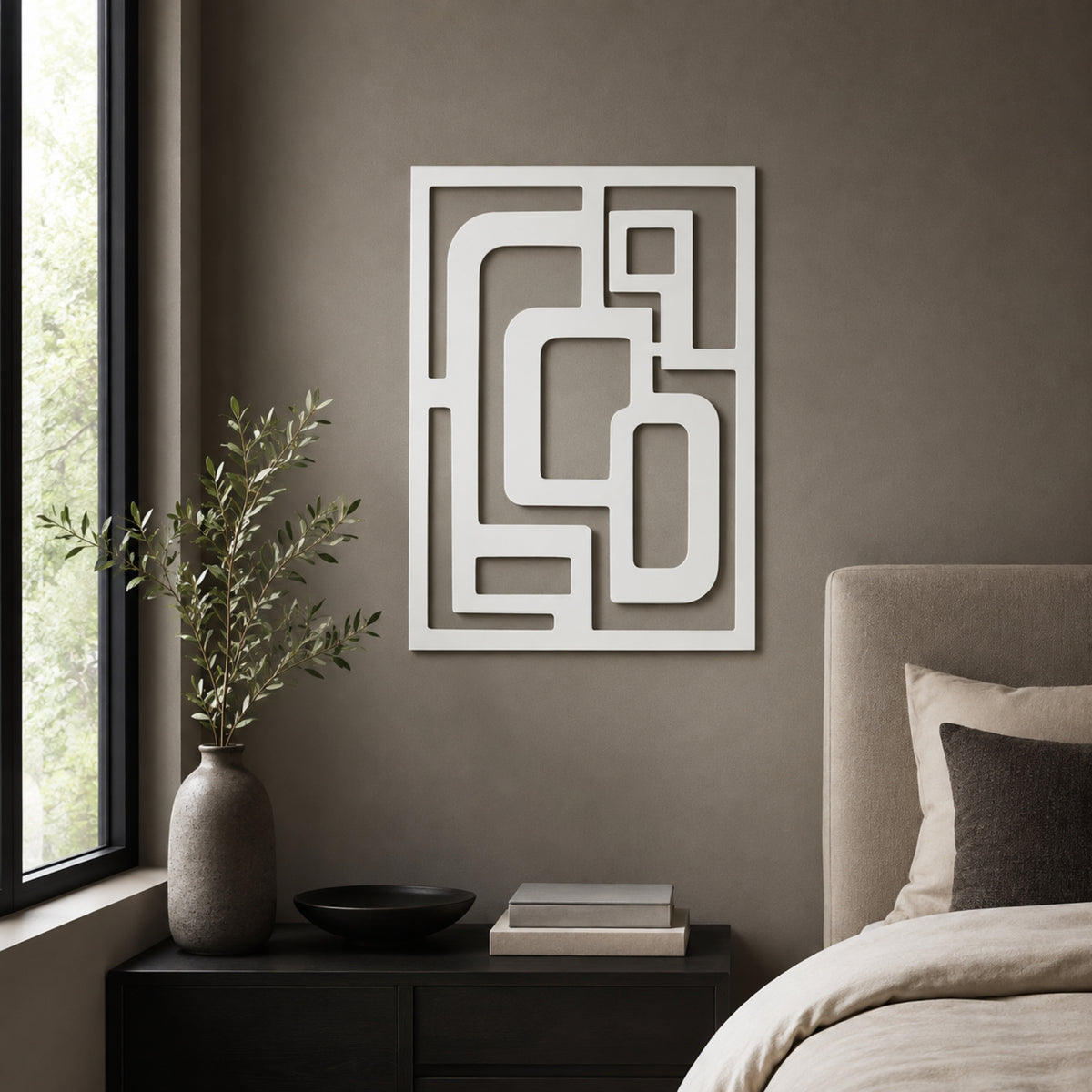 White geometric wall art with an abstract maze-like pattern, displayed on a textured taupe-gray wall above a dark nightstand in a modern bedroom setting.