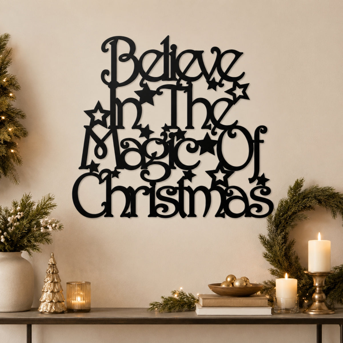 Black metal wall art with the phrase 'Believe in the Magic of Christmas' in decorative script and star motifs, displayed on a beige wall above a styled holiday console with candles, greenery, and a small tree.